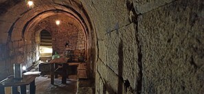 Um corredor de pedra arqueado com uma mesa de madeira e bancos, uma luminária pendente e uma parede de pedra.