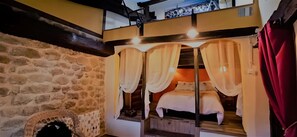 Una habitación acogedora con pared de piedra, cama de madera con cortinas y una silla de mimbre.