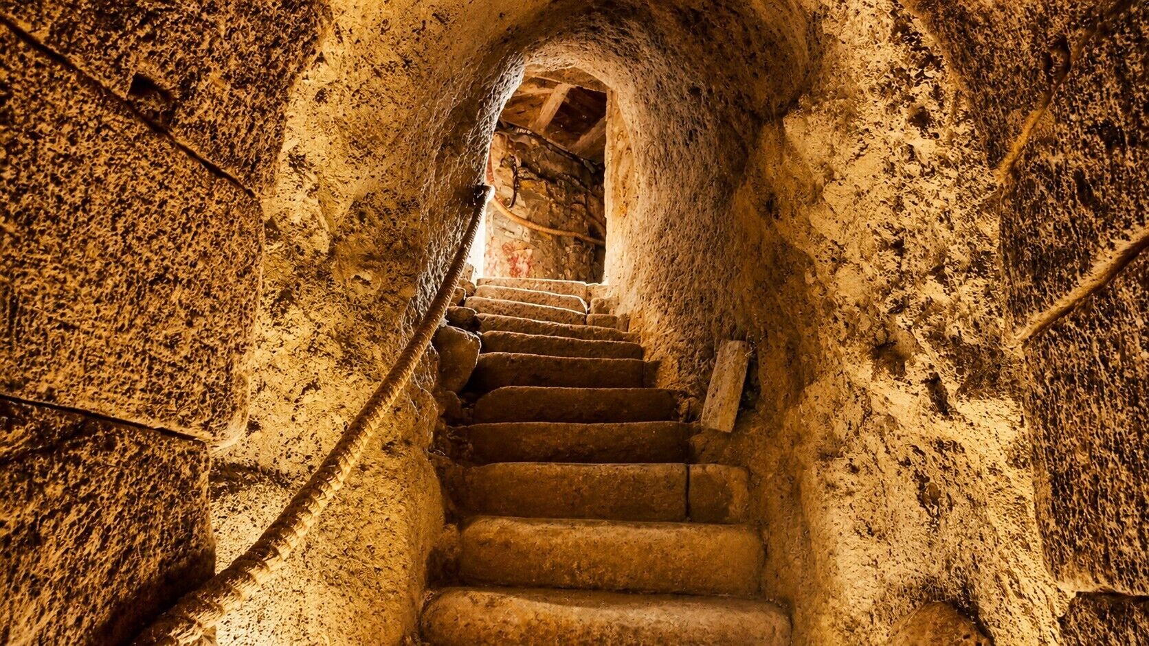 Un escalier en pierre menant vers le haut, dans un passage rustique à arcades.