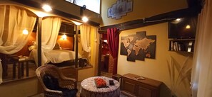 Een gezellige kamer met een bed, een stoel, een klein tafeltje met een schaal fruit en een wereldkaart aan de muur.