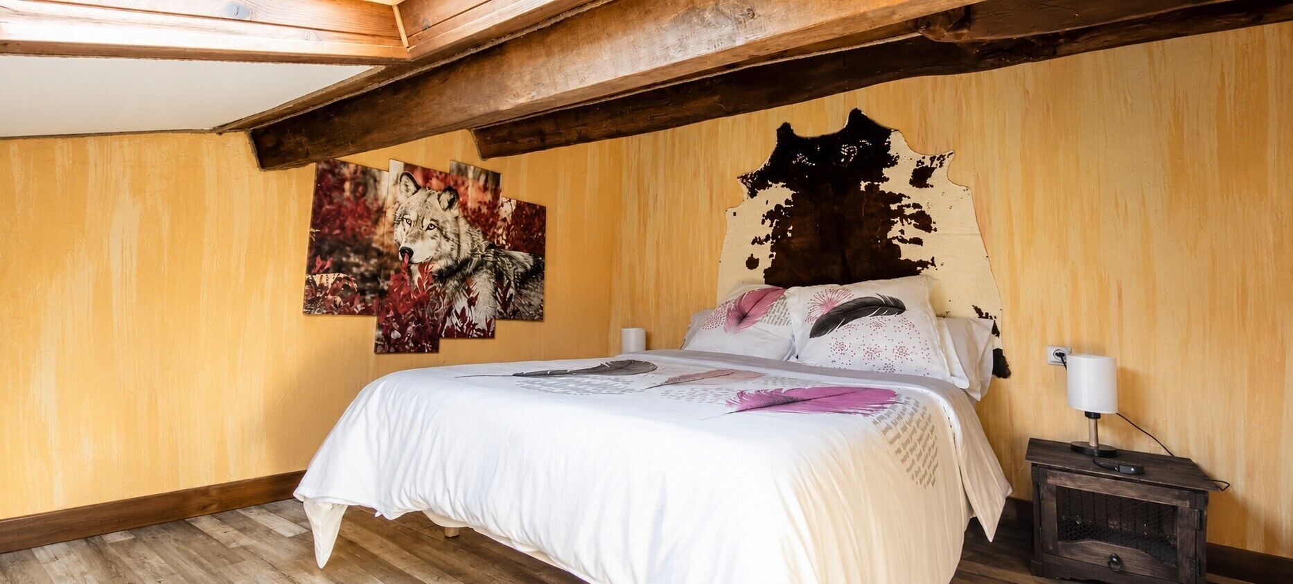 Un dormitorio con una cama, cabecera de madera, mesita de noche y una pared con un cuadro.