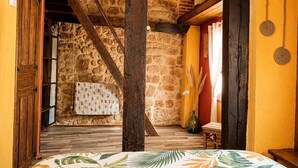 A narrow hallway with a wooden door, a stone wall, and a bed with a floral bedspread.
