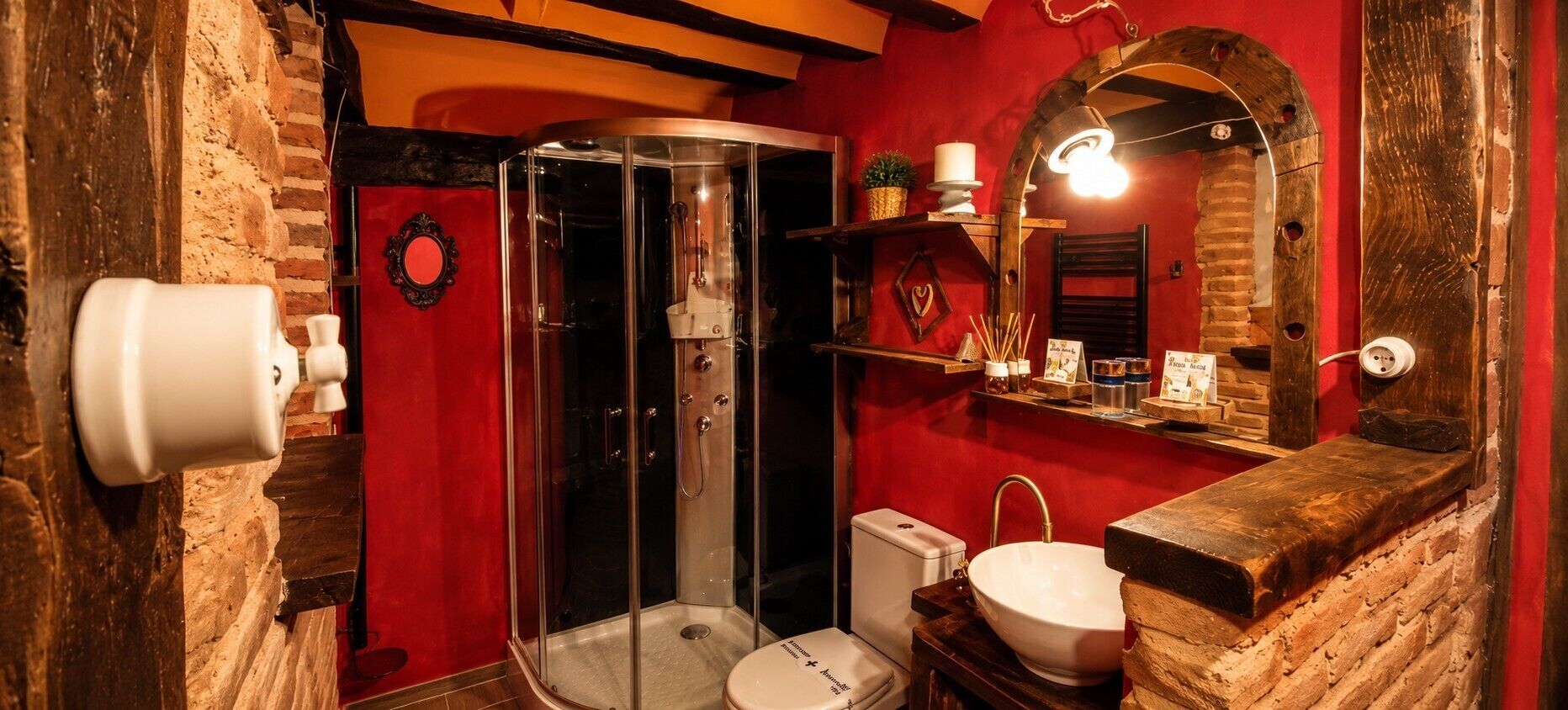 A bathroom with a glass-enclosed shower, a white toilet, a sink with a wooden countertop, and a mirror with a rustic frame.
