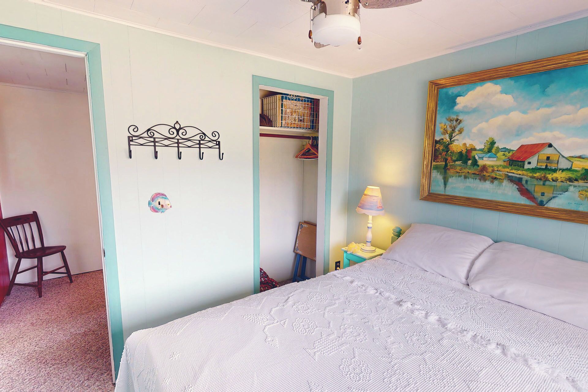 A bedroom with a bed, a chair, a painting, and a ceiling fan.