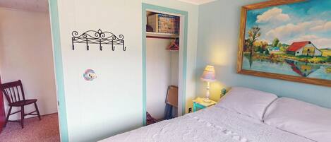 A bedroom with a bed, a chair, a painting, and a ceiling fan.