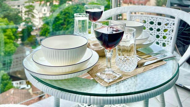Une table à manger, avec des assiettes, des verres et une bouteille, est dressée sur un balcon offrant une vue sur la ville.