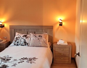 A bedroom with a wooden headboard, two bedside tables with lamps, a bed with floral bedding, and a nightstand with a towel.