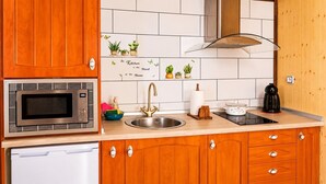 Een keuken met houten kastjes, een roestvrijstalen magnetron, een gootsteen met gouden kraan en een fornuis.