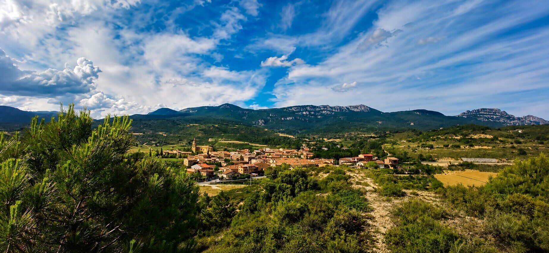 A mountainous landscape with a village featuring traditional architecture, surrounded by greenery and clear skies.