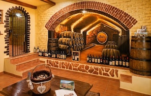A wine cellar with wooden barrels, a brick archway, and a selection of wine bottles on display.