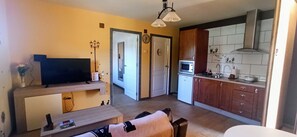 A living room with a TV, a sofa, a coffee table, and a kitchen with cabinets, a microwave, and a sink. - Apartment 'El Guardaviñas Periquita' with Mountain View, Shared Terrace and Wi-Fi (ABALOS)