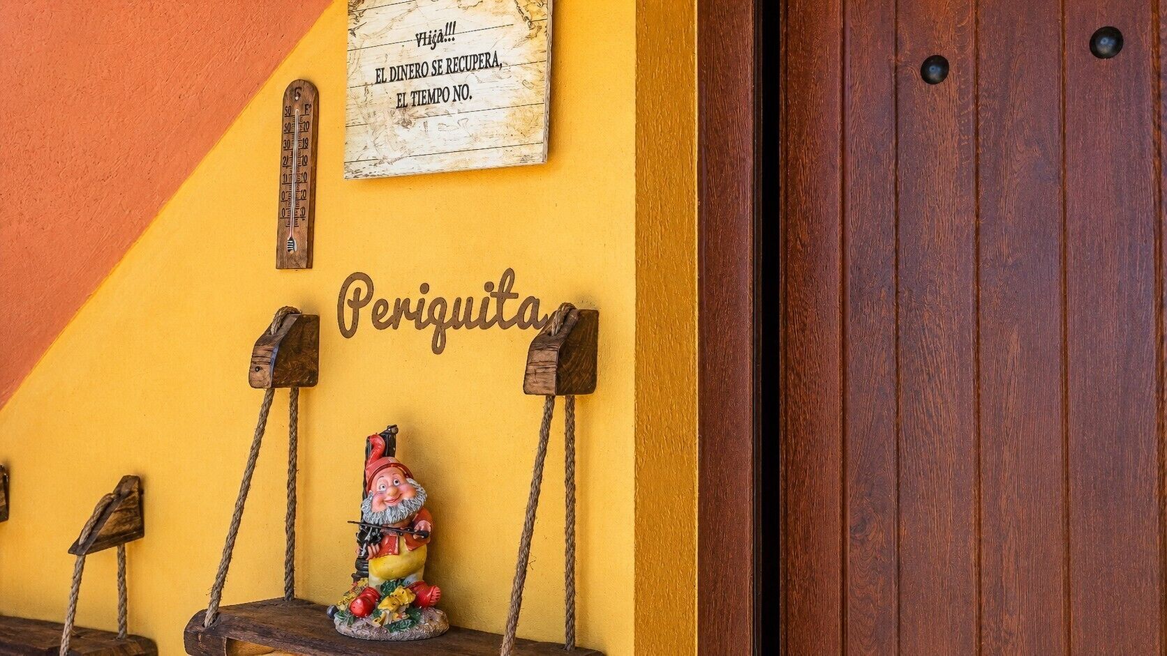 Une porte en bois, avec une enseigne au-dessus, et une petite figurine de gnome posée sur un banc.