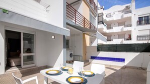 Une terrasse avec une table dressée pour quatre personnes, des chaises blanches et un lave-linge en arrière-plan.