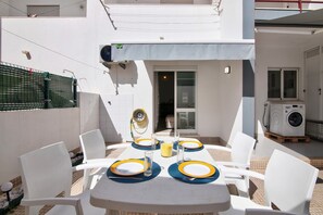 A patio with a table set for four, chairs, and a washing machine in the background.