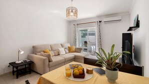 Un salon avec un canapé, une table sur laquelle sont disposés des fruits et une lampe, ainsi qu’un luminaire suspendu.