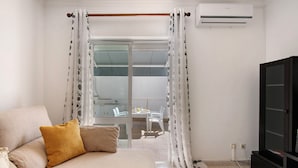 Une pièce comprenant un canapé, un téléviseur et un balcon avec des chaises et une table.