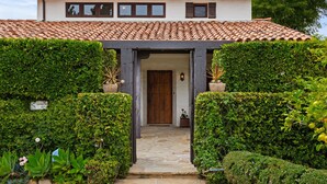 A house with a stone pathway leading to a wooden door, surrounded by well-maintained hedges and potted plants. - Luxurious Garden Home Walking Distance to Downtown SB (Santa Barbara)
