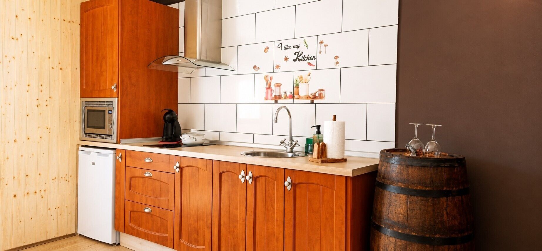 Una cocina con armarios de madera, un microondas, una cafetera, un lavabo y un barril de madera.