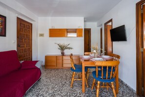 A room with a dining table, chairs, a red sofa, a wooden cabinet, and a television mounted on the wall.