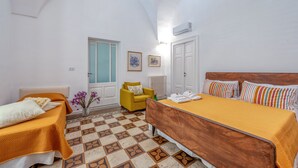 A hotel room with a bed, a chair, a small table, a radiator, and a door. - Sanbiagioapartment with Balcony, Wi-Fi, and Air Conditioning (Lecce)