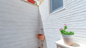 A white brick bathroom with a terracotta sink, a window, and a potted plant on the counter. - Sanbiagioapartment with Balcony, Wi-Fi, and Air Conditioning (Lecce)