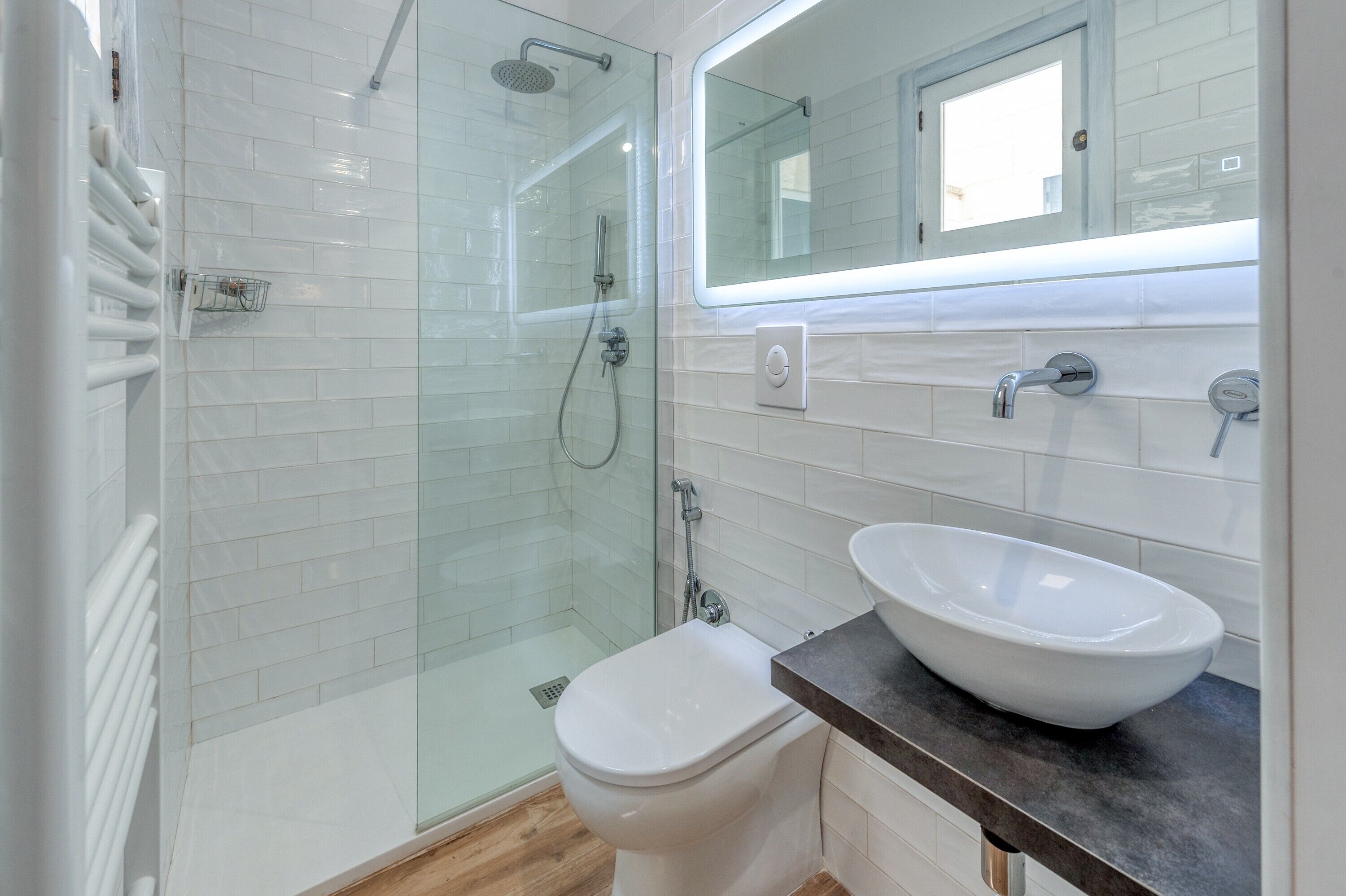 A modern bathroom with a glass-enclosed shower, a white toilet, a large mirror, and a white sink.
