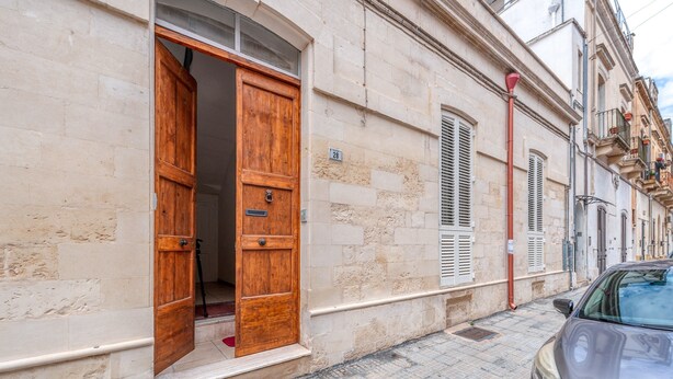 A stone building with a wooden door, a number '28' sign, and a parked car. - Sanbiagioapartment with Balcony, Wi-Fi, and Air Conditioning (Lecce)