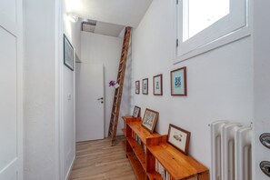 A narrow hallway with a wooden ladder, wooden bookshelves, framed pictures, and a radiator.