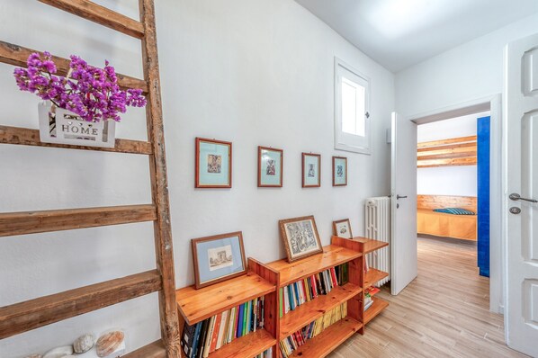 A hallway with a wooden bookshelf, framed pictures, and a bed in the background.
