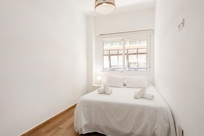 A minimalist bedroom with a large window, a bed with white linens, and a bedside table with a lamp.