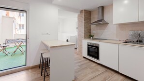 Une cuisine moderne dotée d’un îlot central, d’un four encastré et d’une grande fenêtre donnant sur une cour.