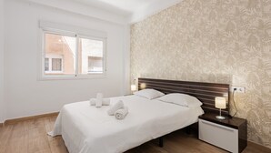 Un lit bien fait, avec des serviettes pliées, une table de chevet avec une lampe, une fenêtre avec des stores et un papier peint à motifs.