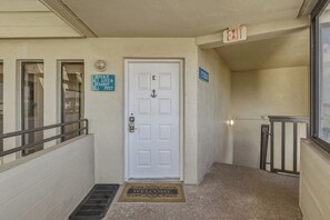 A white door with a mail slot, a welcome mat, a blue sign with 'PEACE LOVE & SANDY FEET', and an exit sign.