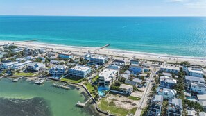 An aerial view of a coastal residential area with houses, a beach, and a marina.