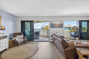A modern living room with a sofa, a chair, a lamp, a bookshelf, and a view through glass doors to an outdoor patio.