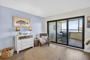 A room with a white dresser, a chair, a round rug, and a view through a sliding glass door to an outdoor seating area.