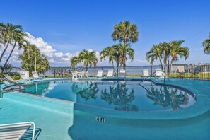 A clear blue pool with lounge chairs and palm trees, surrounded by a fence. - Bayview Condo, Unit E - Anna Maria Island - 2 Bedroom/ 2 Bath bay view, maximum occupancy of 4 people. (Bradenton Beach)