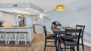 Una cocina moderna con una isla central, taburetes de bar, una mesa de comedor con sillas e iluminación colgante.