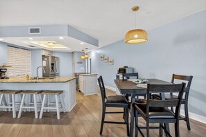 A modern kitchen with a central island, bar stools, a dining table with chairs, and pendant lighting. - Bayview Condo, Unit E - Anna Maria Island - 2 Bedroom/ 2 Bath bay view, maximum occupancy of 4 people. (Bradenton Beach)
