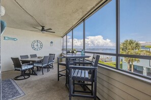 A balcony with a table and chairs, a clock, and a view of the ocean.