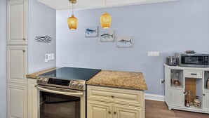 Una cocina con estufa, microondas y armarios. Hay luces empotradas en la pared y obras de arte.