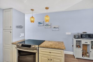 A kitchen with a stove, microwave, and cabinets. There are wall-mounted lights and artwork. - Bayview Condo, Unit E - Anna Maria Island - 2 Bedroom/ 2 Bath bay view, maximum occupancy of 4 people. (Bradenton Beach)