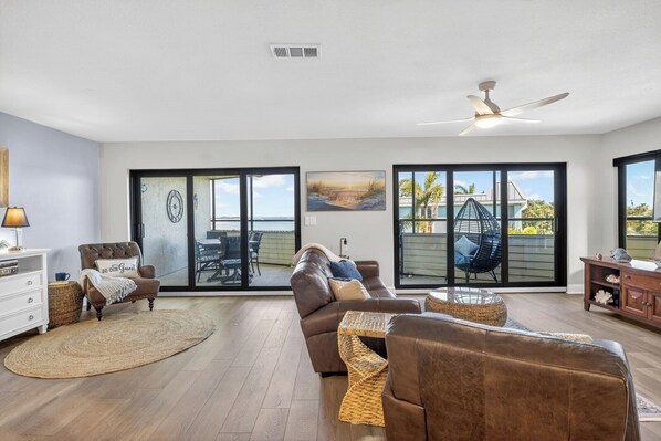 Ein großzügiges Wohnzimmer mit einer braunen Ledersofa, einem runden Couchtisch und einem Essbereich mit Tisch und Stühlen. Ein Glastür führt auf einen Balkon mit Blick auf das Meer.