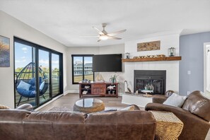 A living room with a fireplace, a television, and a large window overlooking a balcony. - Bayview Condo, Unit E - Anna Maria Island - 2 Bedroom/ 2 Bath bay view, maximum occupancy of 4 people. (Bradenton Beach)