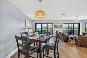 A modern dining area with a table, chairs, and a hanging light fixture. - Bayview Condo, Unit E - Anna Maria Island - 2 Bedroom/ 2 Bath bay view, maximum occupancy of 4 people. (Bradenton Beach)
