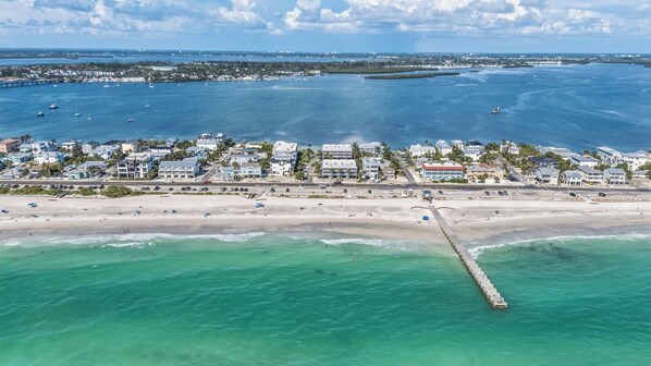 An aerial view of a coastal town with a beach, waterfront buildings, and a pier extending into the water.