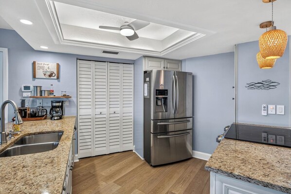 A modern kitchen with a stainless steel refrigerator, granite countertops, a built-in oven, and a ceiling fan.