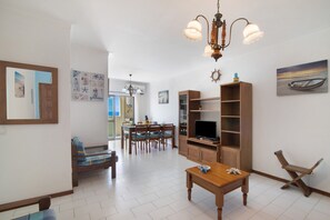 A living room with a wooden table, a sofa, a TV stand, and a dining area with chairs and a table.