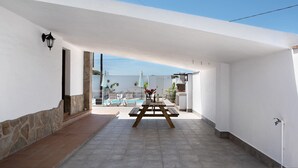 A patio area with a wooden table and chairs, a stone wall, and a pool in the background. - Holiday Home 'El Cortijo' with Private Pool, Wi-Fi and Air Conditioning (Conil de la frontera)