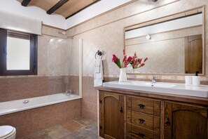 A bathroom with a bathtub, shower, vanity with a mirror, and a window.